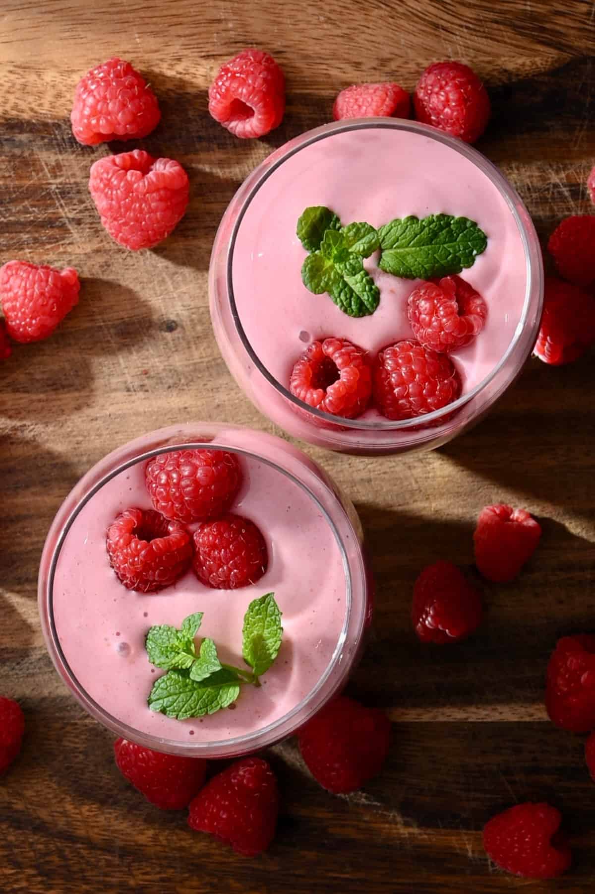 Top view of two glasses with pink smoothie topped with raspberries