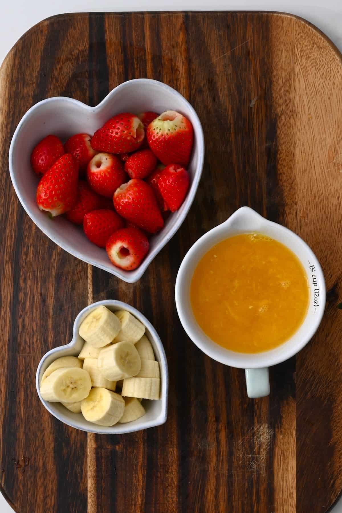 A bowl with strawberries a bowl with chopped banana and a bowl with orange juice