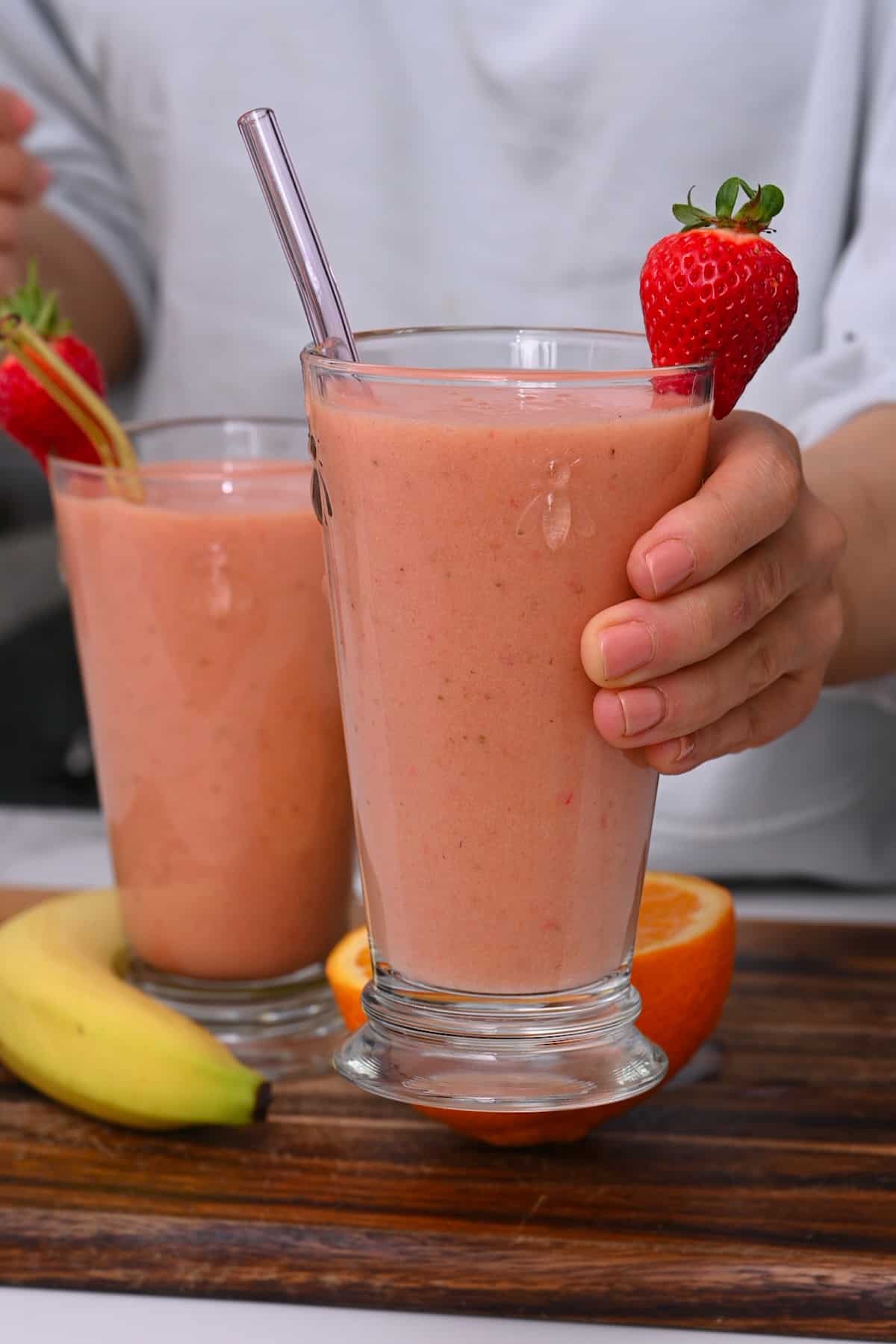 Hand holding a glass with strawberry smoothie topped with a strawberry