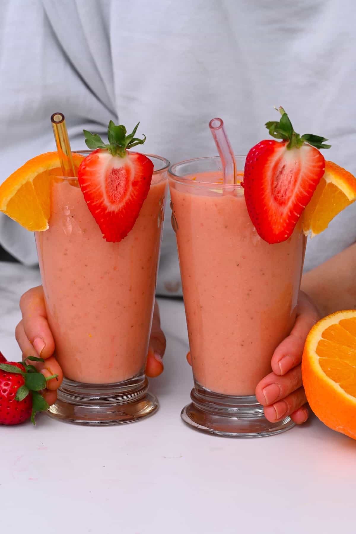 Two galsses with smoothies topped with strawberries and orange slices