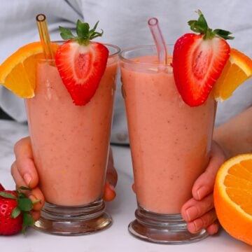 Two galsses with smoothies topped with strawberries and orange slices