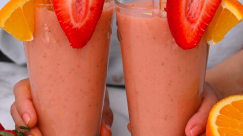 Two galsses with smoothies topped with strawberries and orange slices