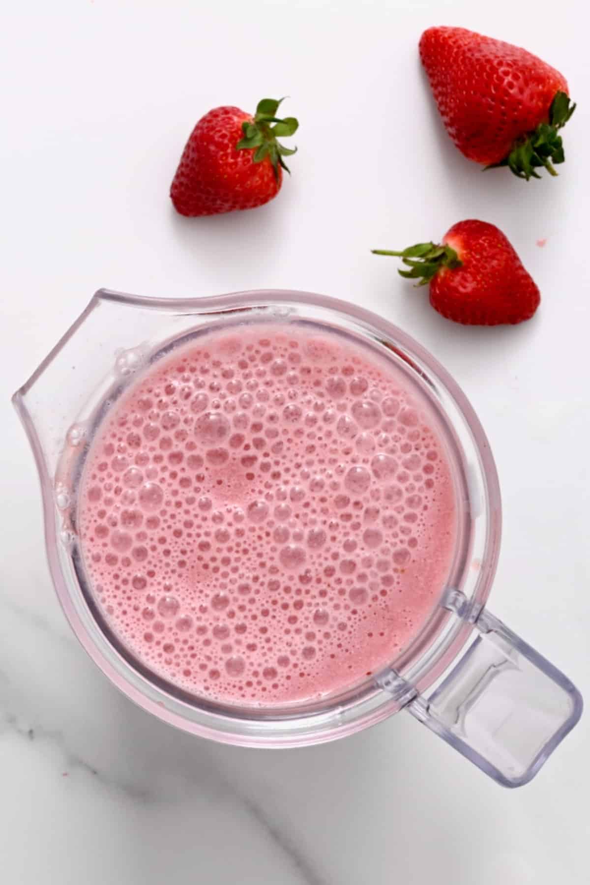 Strawberry milk in a blender and three strawberries next to it