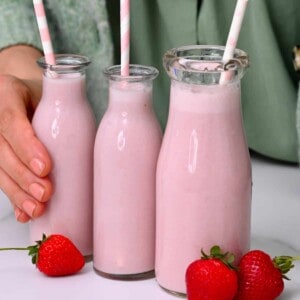 Three bottles with strawberry milk and straws and three strawberries next to them