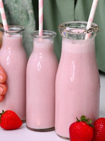 Three bottles with strawberry milk and straws and three strawberries next to them