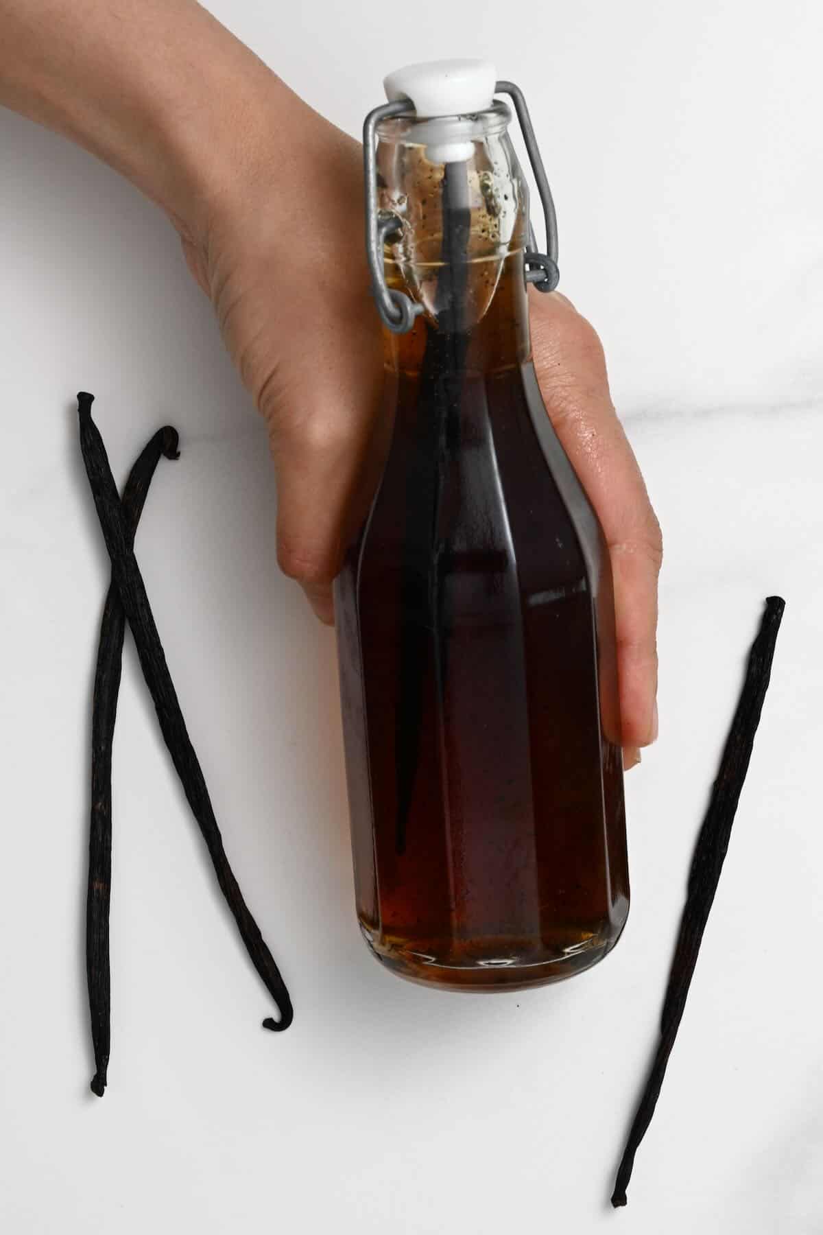 A bottle with homemade vanilla syrup and three vanilla beans next to it