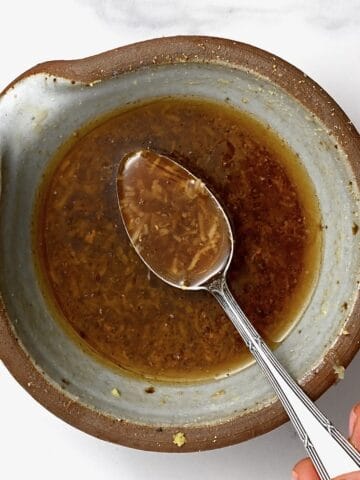 A spoonful of asian salad dressing over a bowl