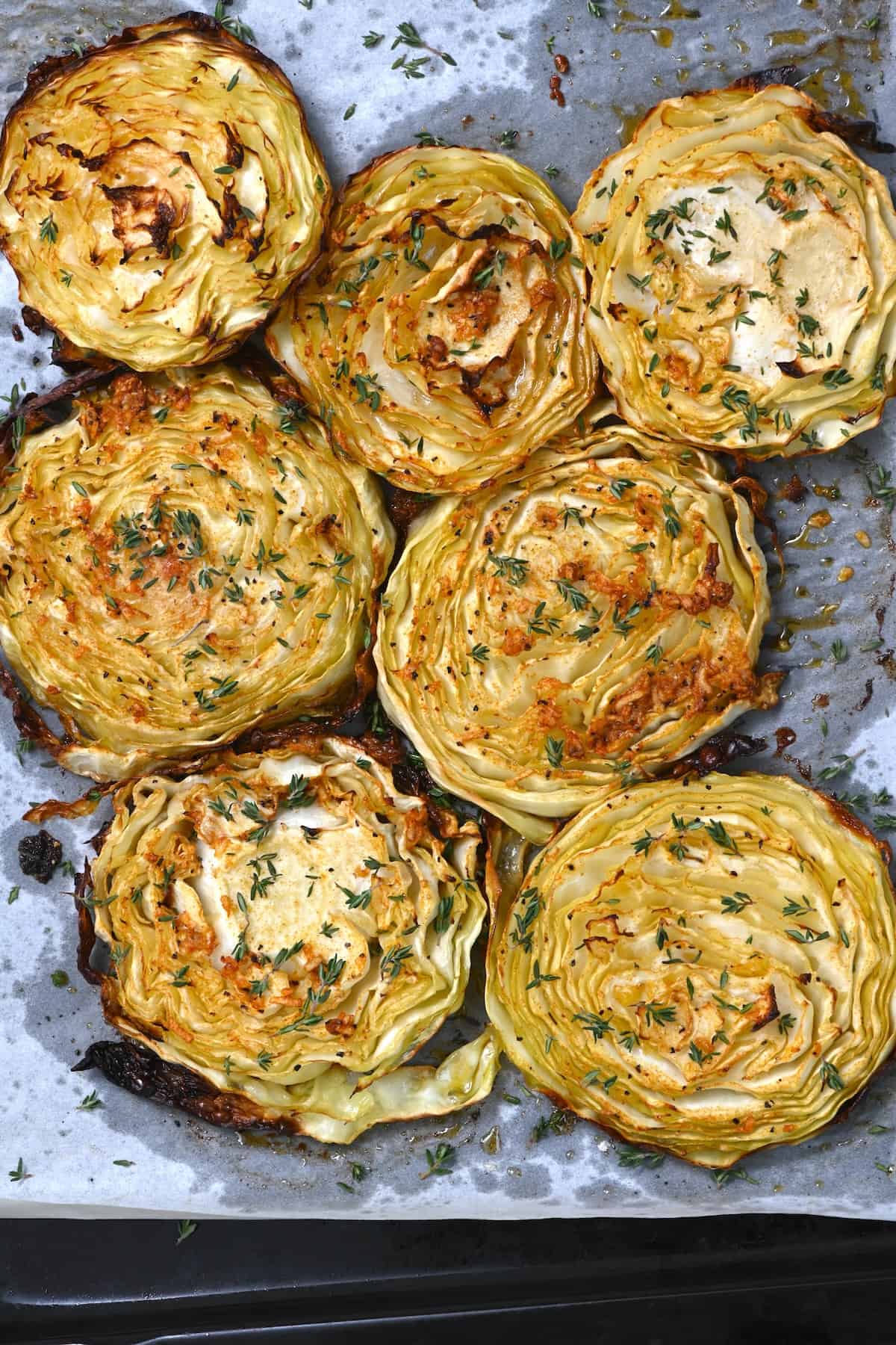 Seven cabbage steaks topped with thyme on a tray
