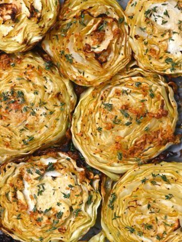 Seven cabbage steaks topped with thyme on a tray