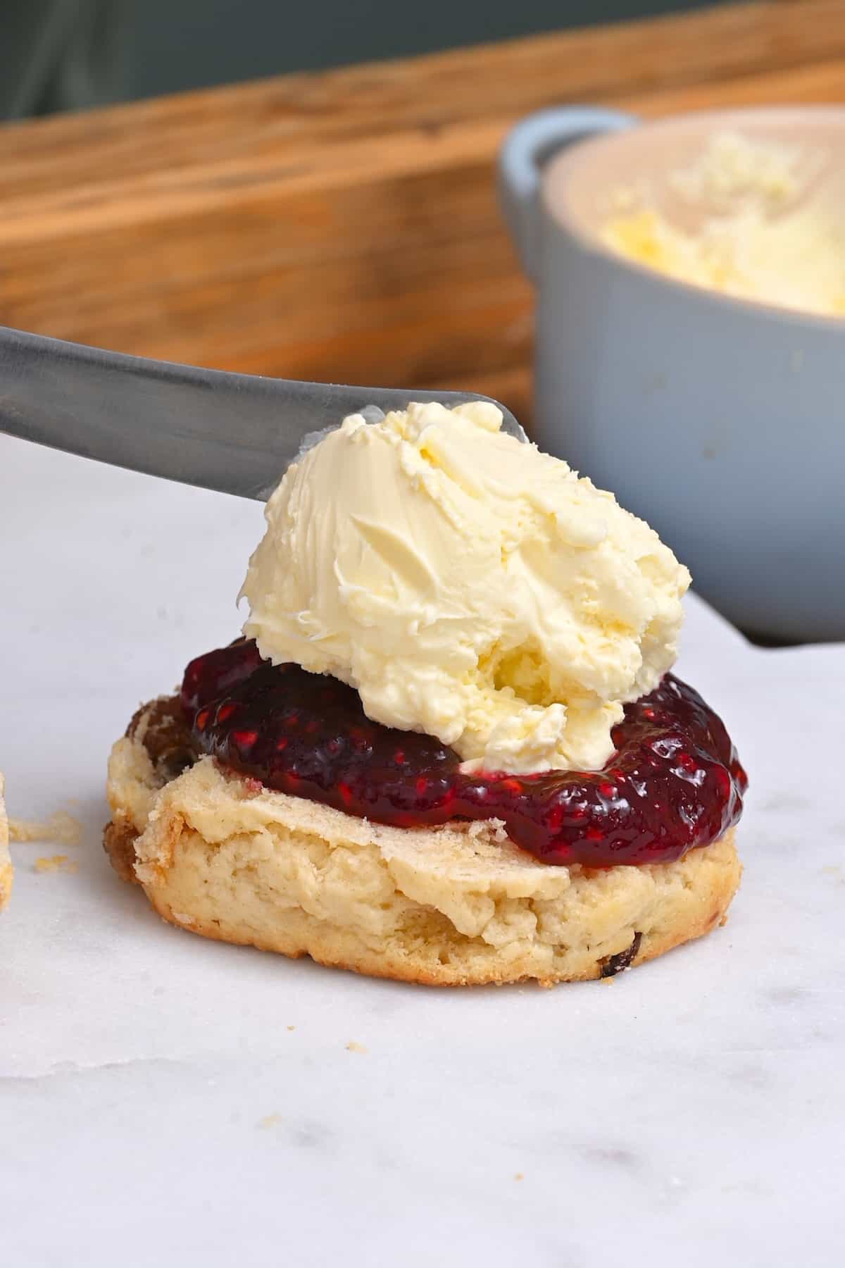 Homemade clotted cream topping raspberry jelly on a scone