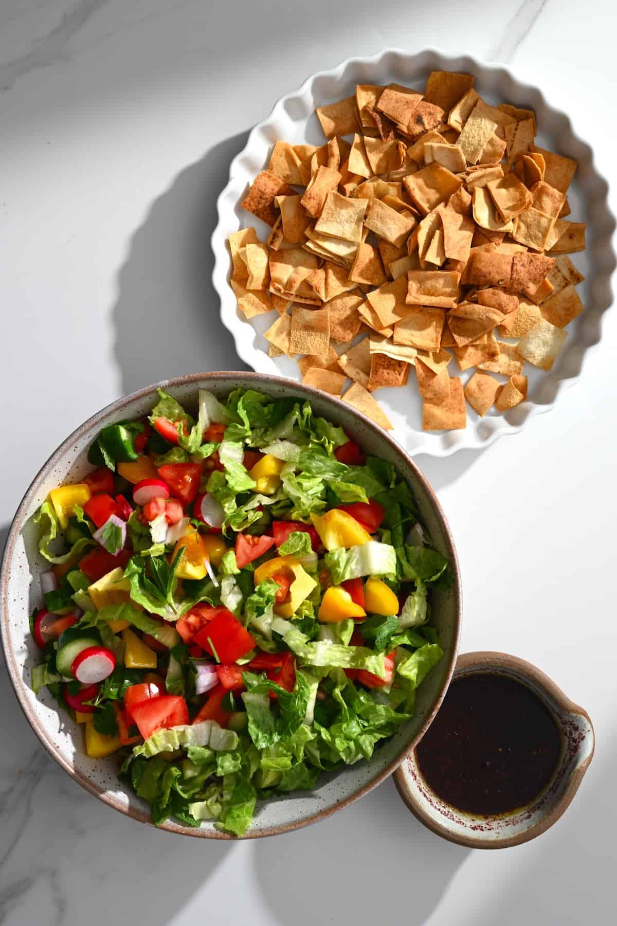 Fattoush salad in a bowl with the dressing and pita chips apart