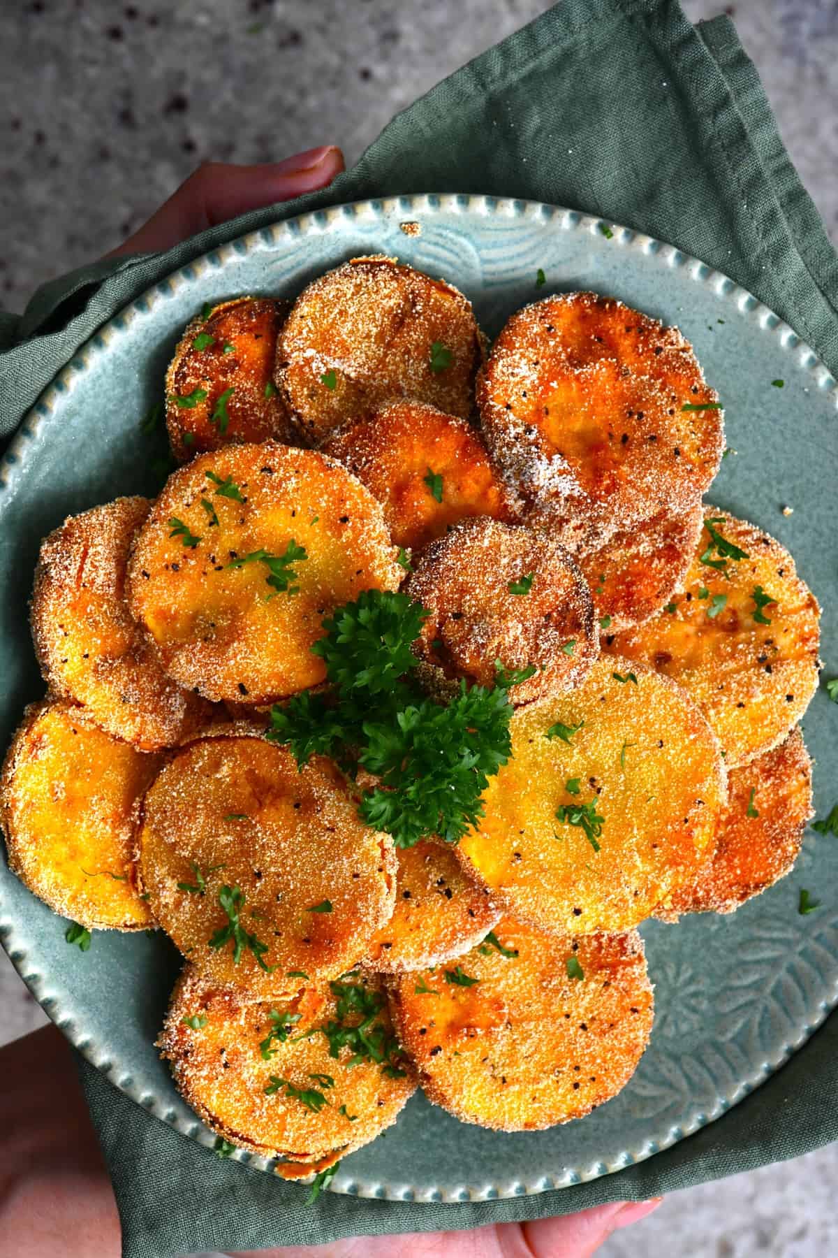 Freshly fried slices of yelloe squash on a plate topped with parsley