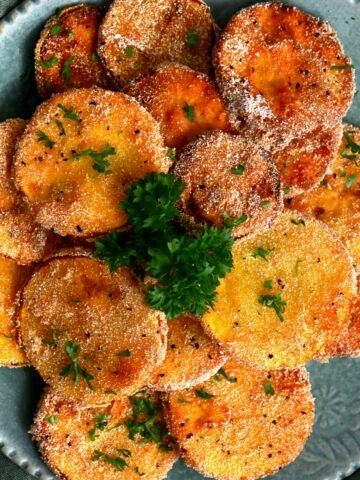 Freshly fried slices of yelloe squash on a plate topped with parsley