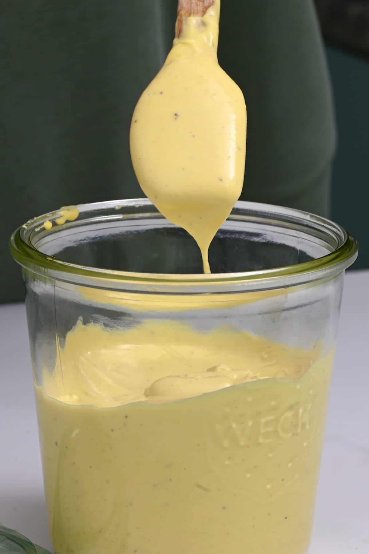 Spoonful of garlic mayo driping over a jar