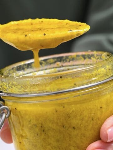 Homemade ginger salad dressing dripping from a spoon over a jar
