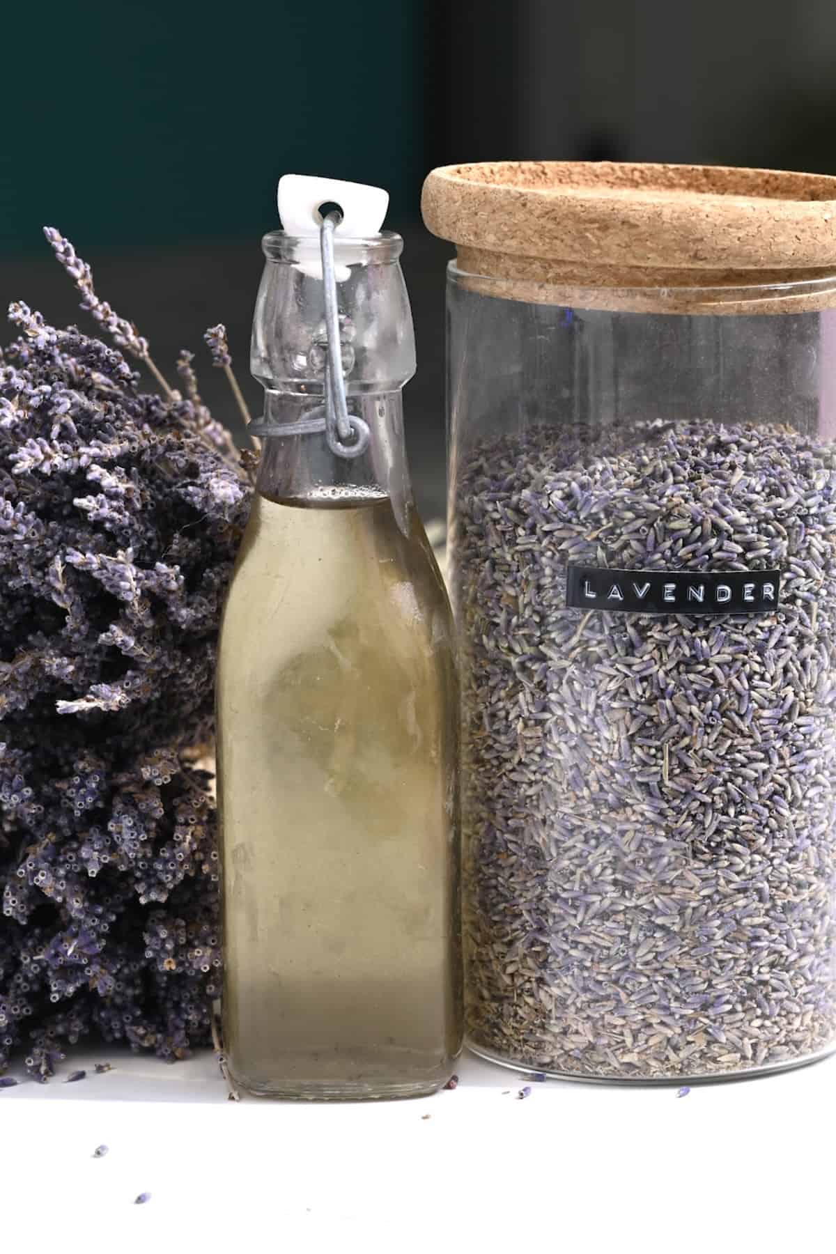 Lavender syrup in a bottle next to a jar with lavender petals