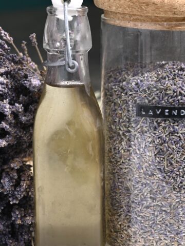 Lavender syrup in a bottle next to a jar with lavender petals