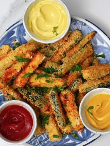 A plate with zucchini fries and three dips in little bowls