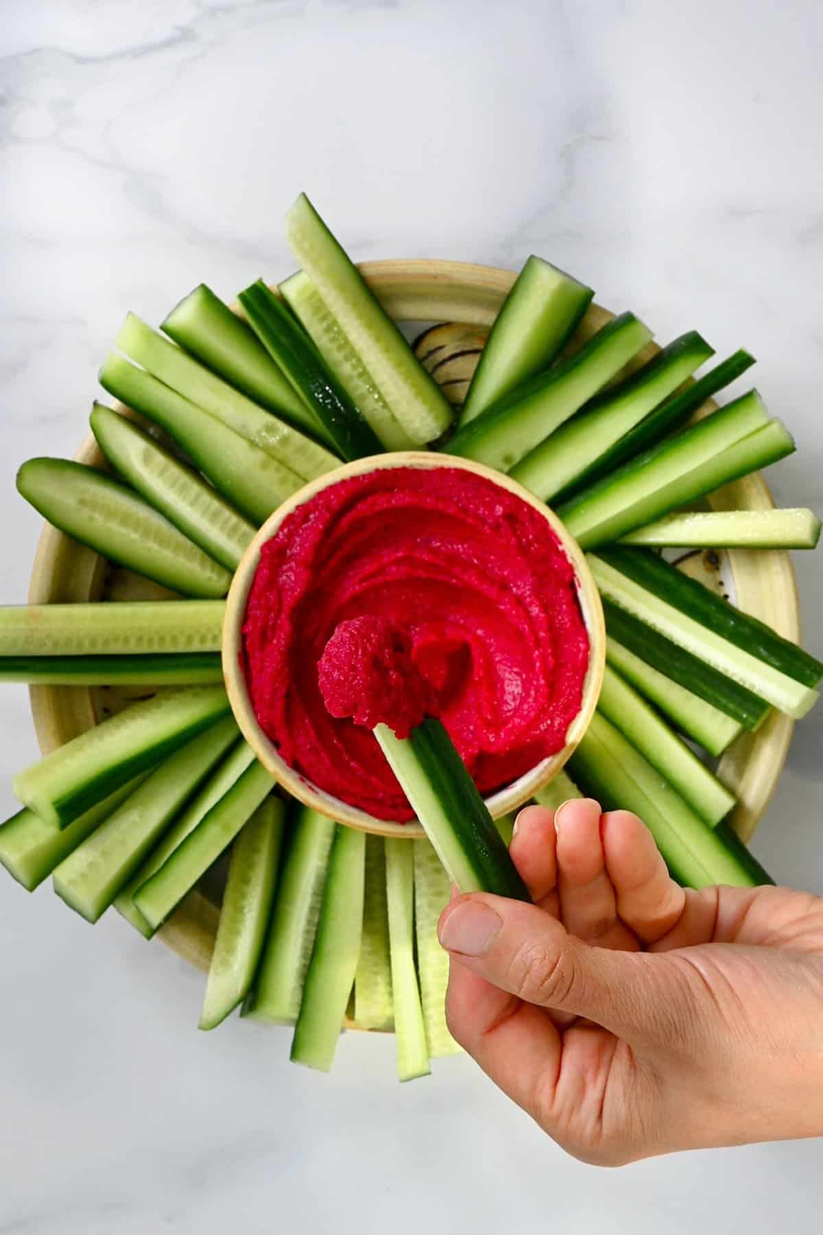 Eating beet hummus with a cucumber stick