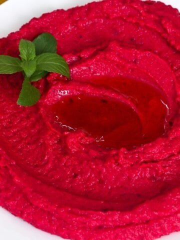 Beet hummus on a plate topped with mint laves