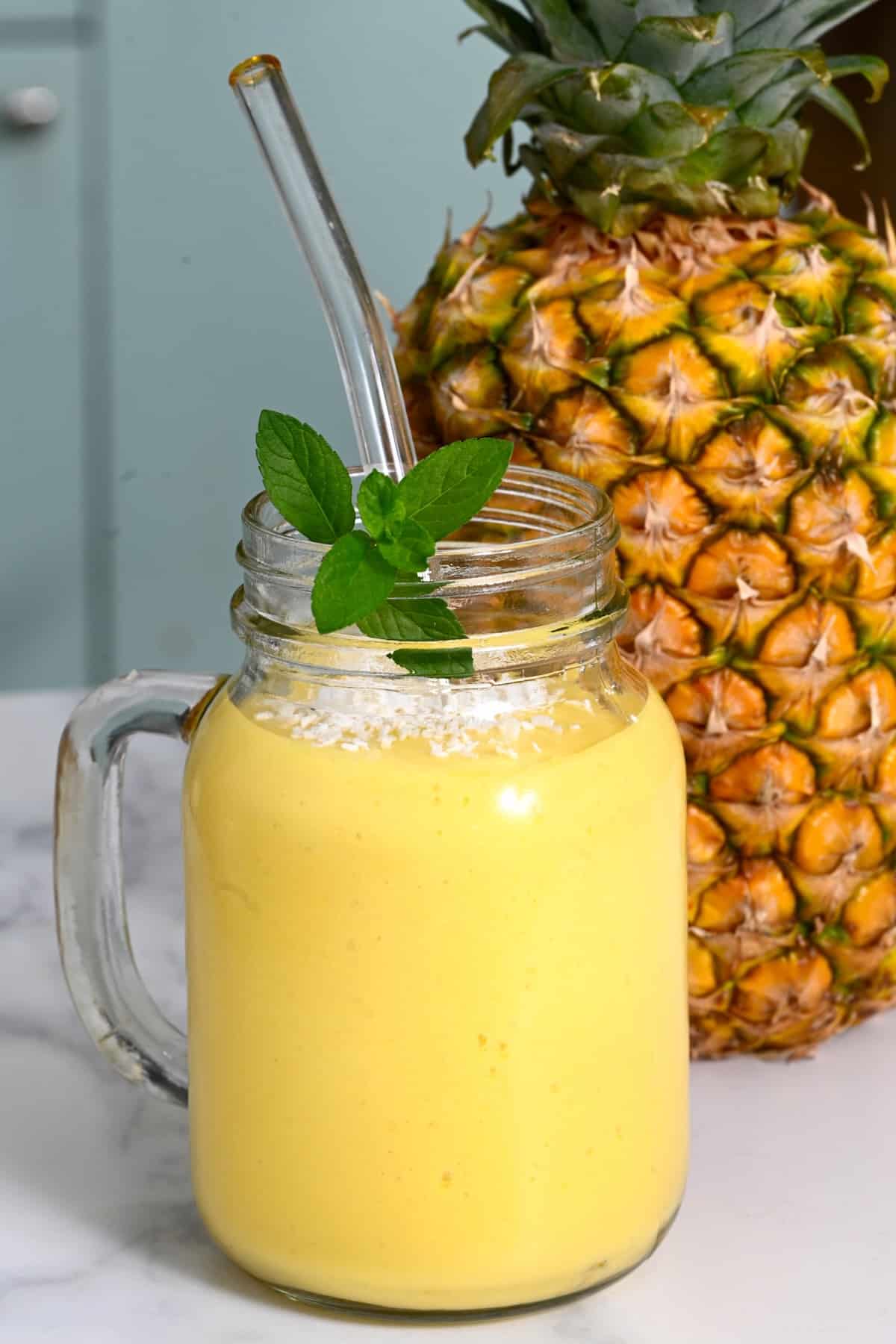 Pineapple mango smoothie with a straw and mint leaves