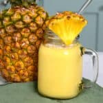 Mango pineapple smoothie in a jar with a glass straw and pineapple slice