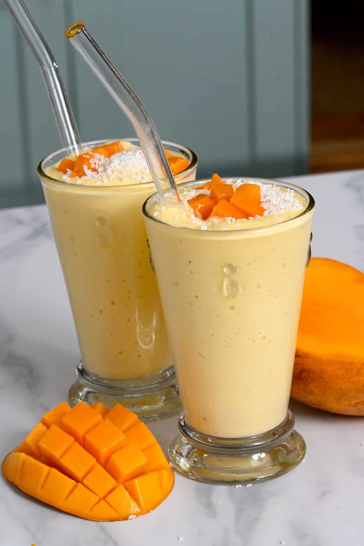 Two glasses with mango smoothie topped with coconut shreds