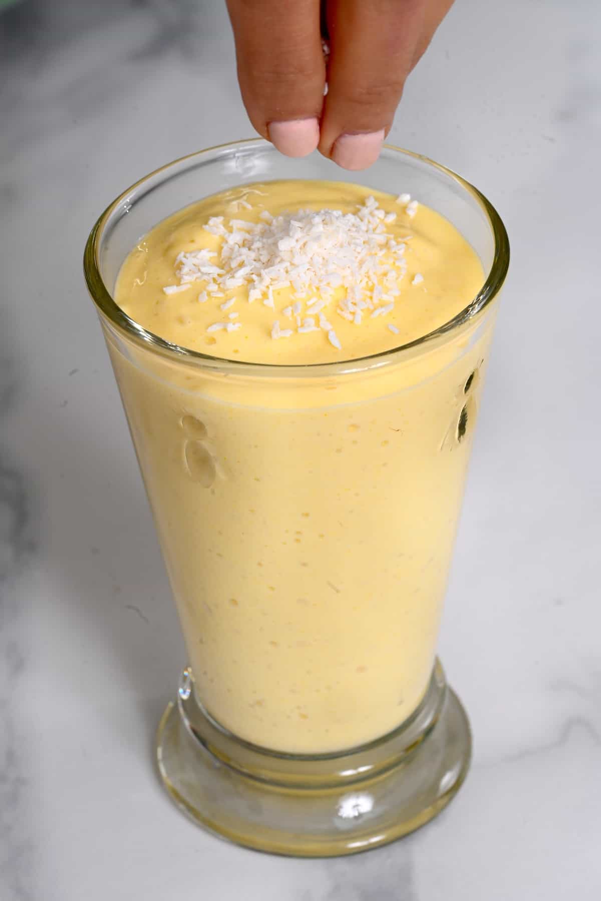 Topping mango smoothie with coconut shreds