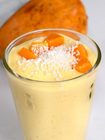 A glass with mango smoothie topped with coconut shreds