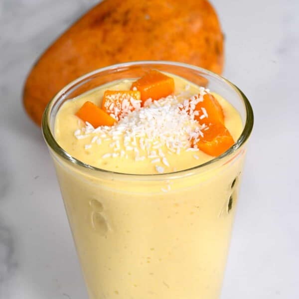 A glass with mango smoothie topped with coconut shreds
