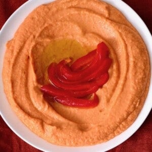 A plate with roasted red pepper hummum topped with peppers