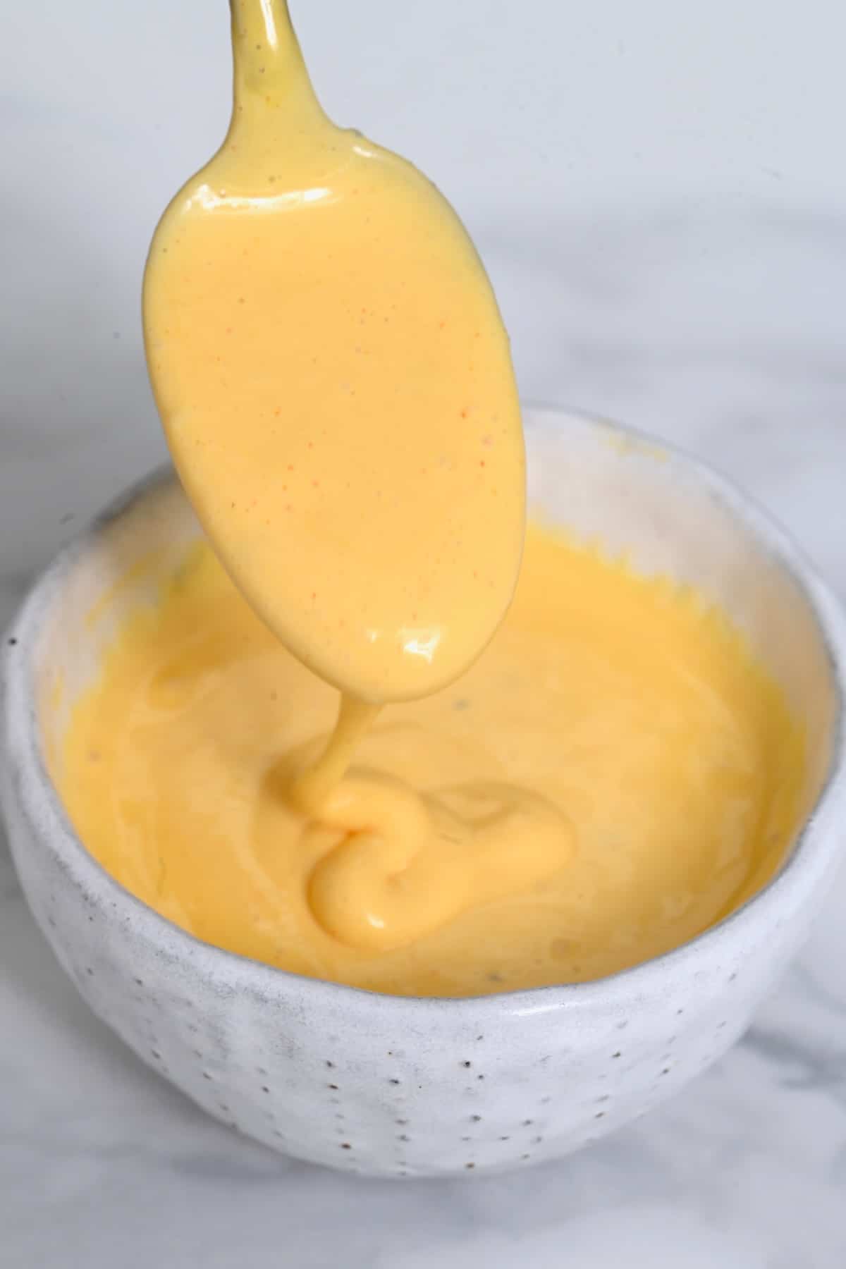A spoonful with Hollandaise sauce dripping over a small bowl