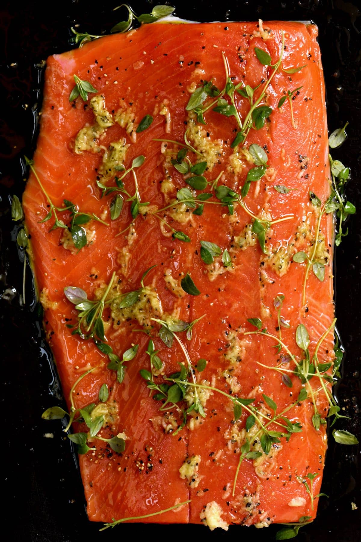 Raw salmon topped with minced garlic and herbs on baking tray