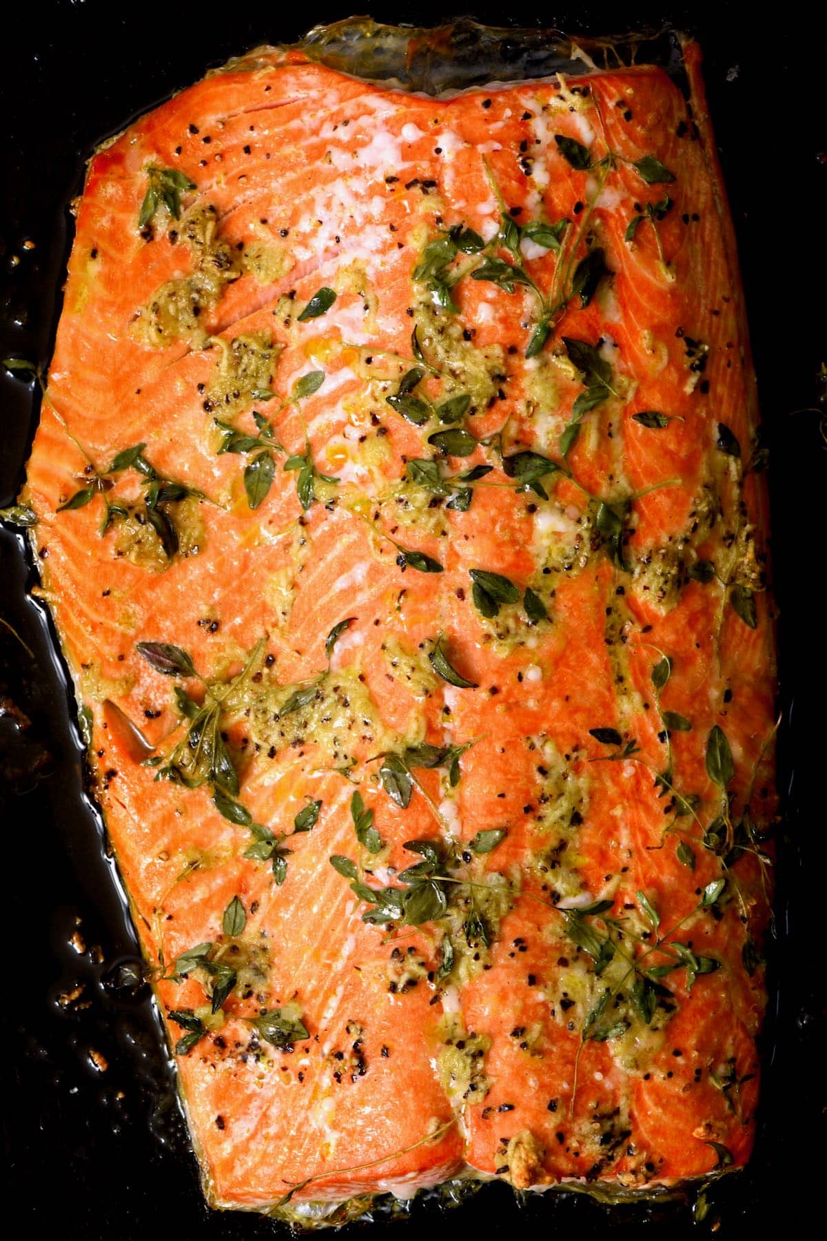 baked salmon topped with minced garlic and herbs on baking tray