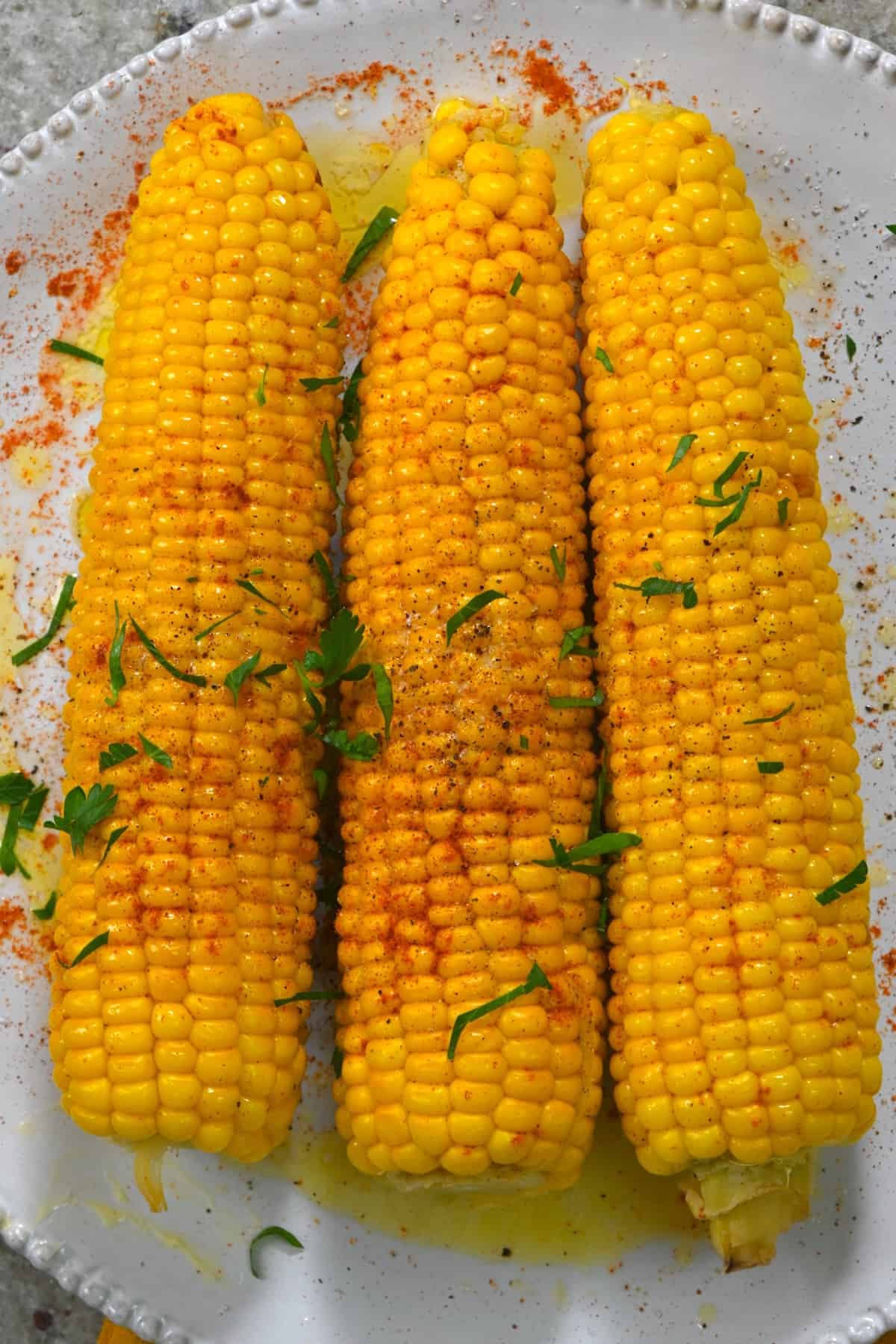Three boiled corn on the cob topped with butter and pepper