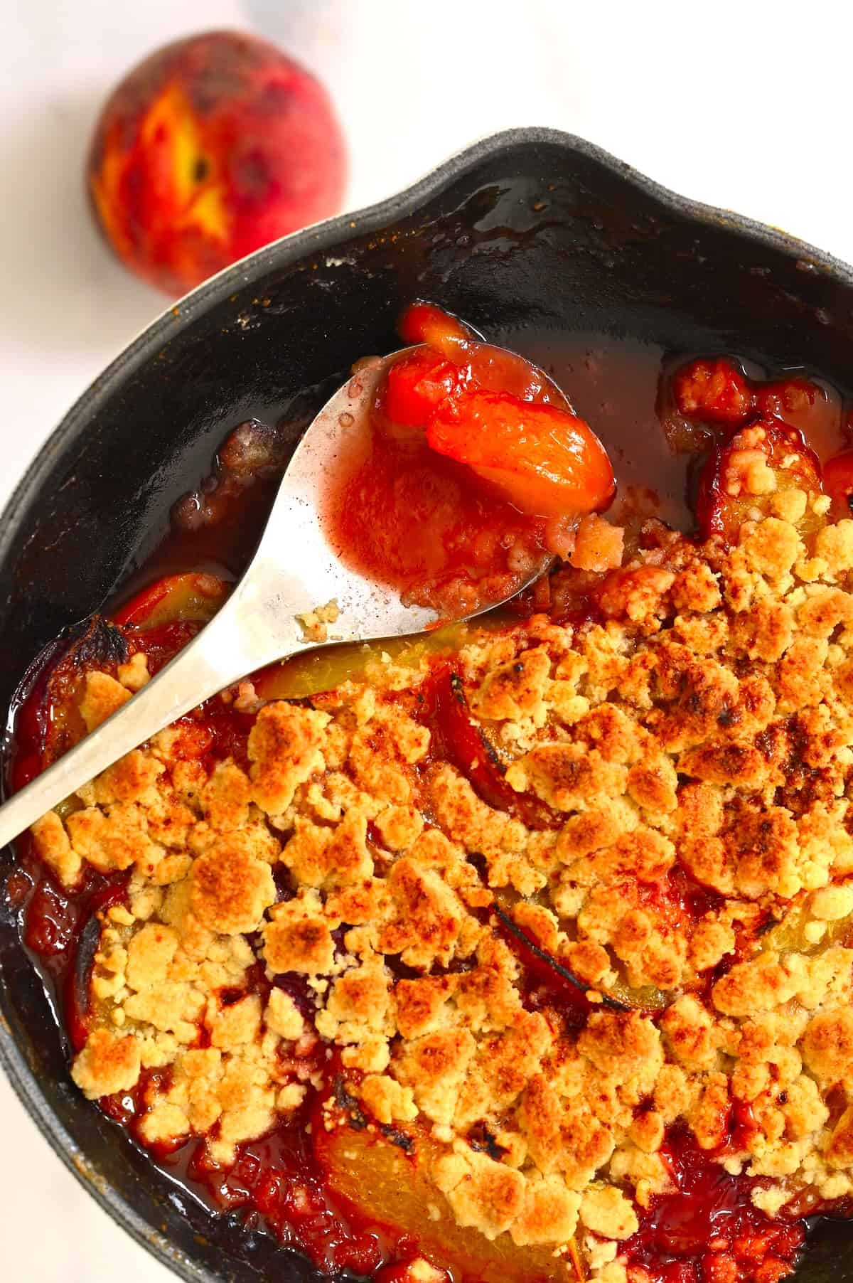 A spoonful of peach crumble over a baking dish