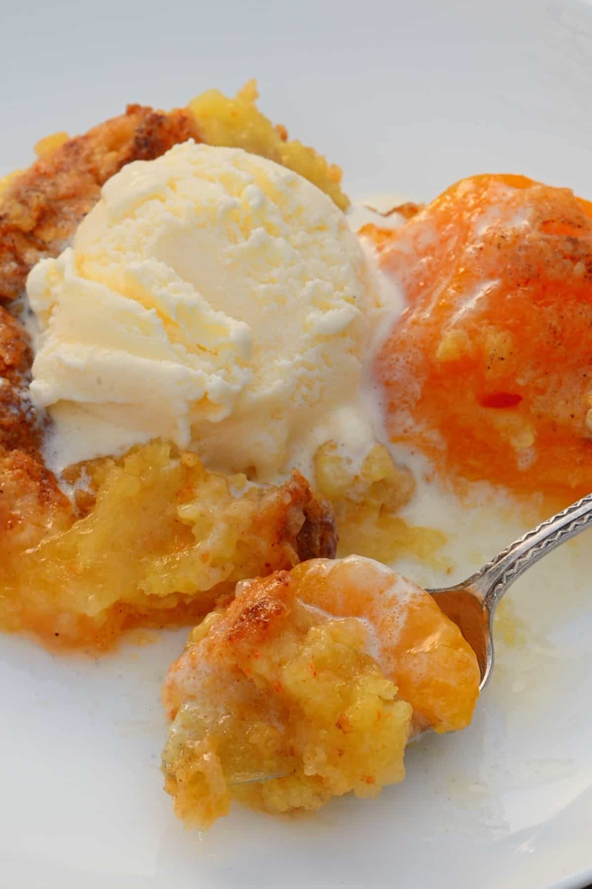 A spoonful and a serving of peach dump cake and ice cream