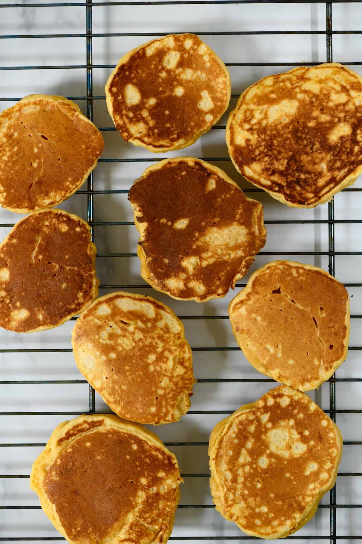 Nine ricotta pancakes resting on a grill