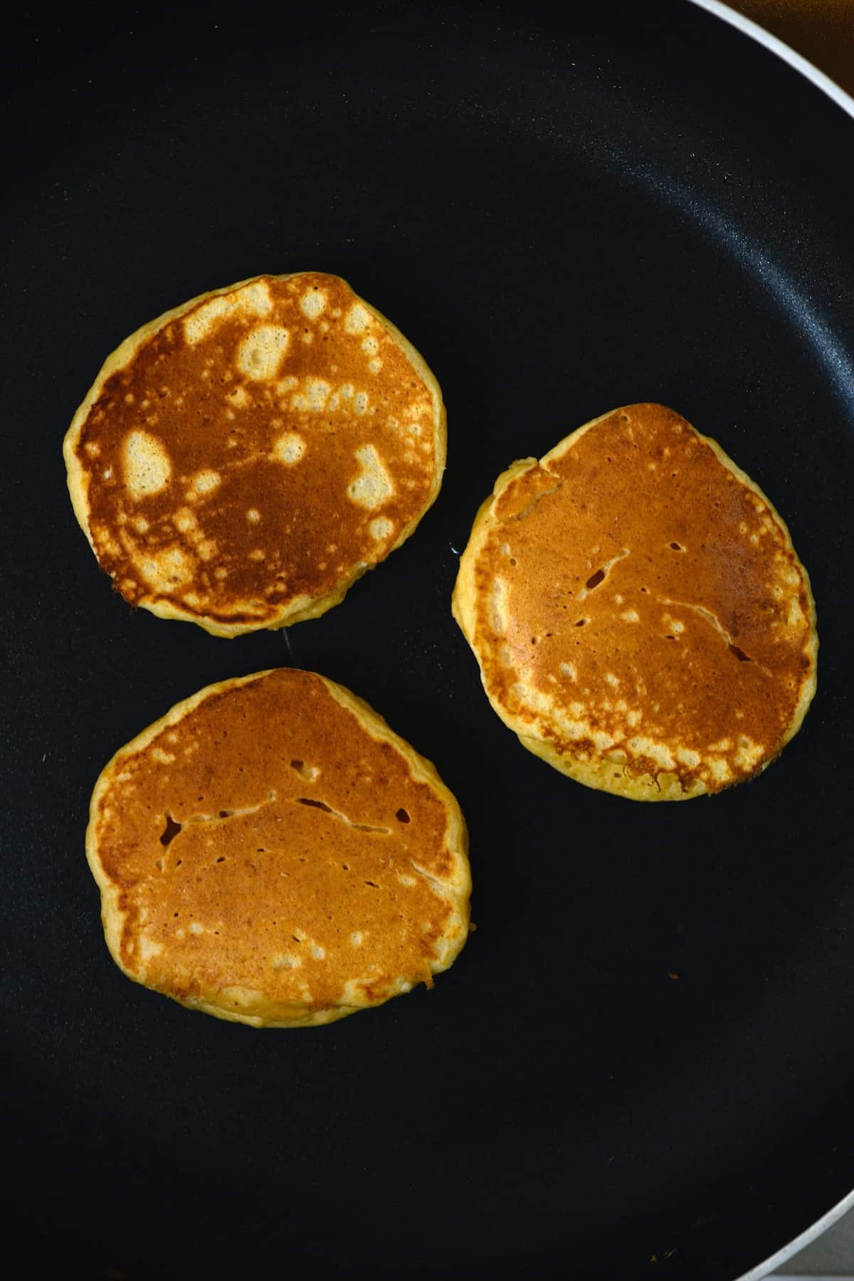 Three freshly made ricotta pancakes on a pan