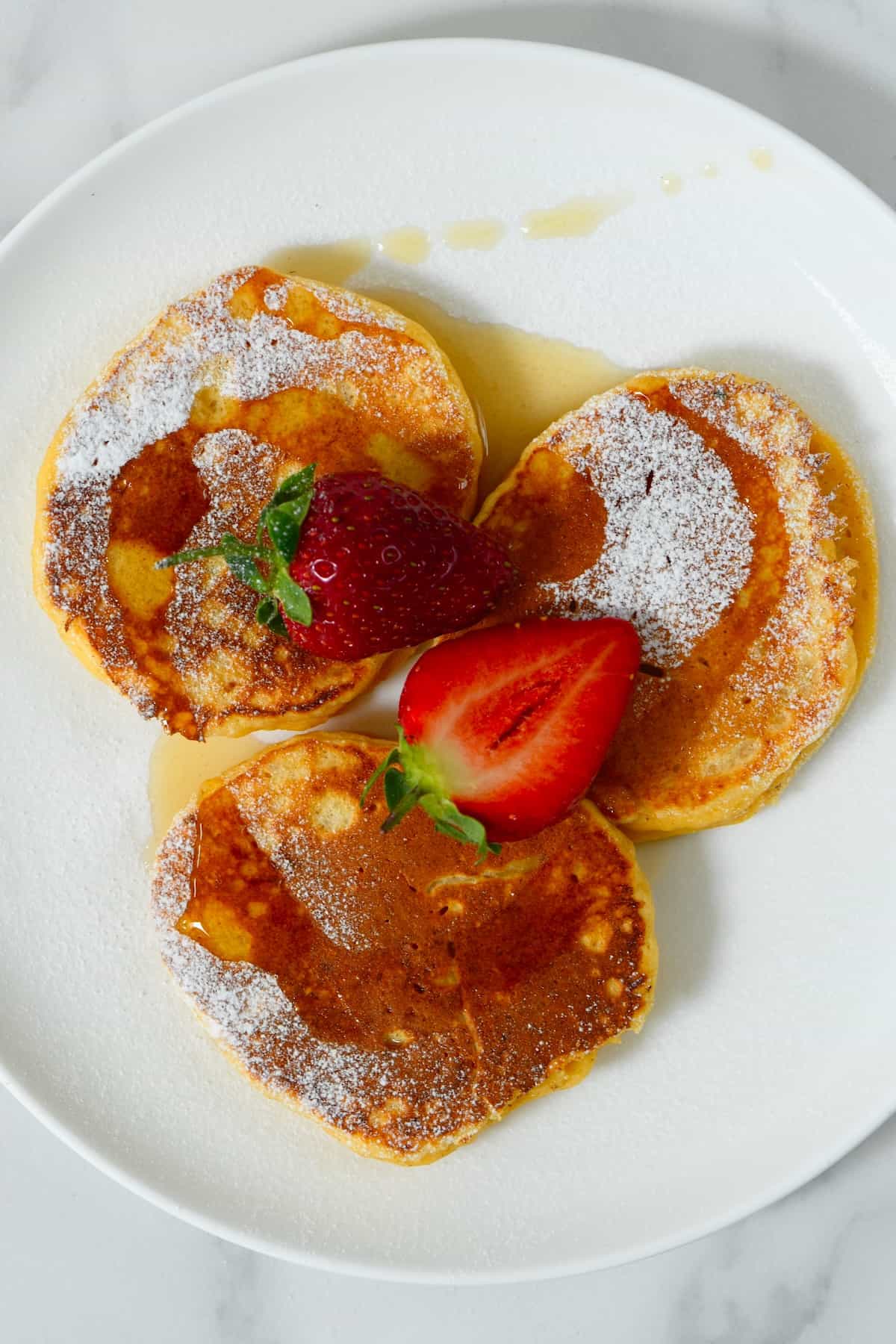 Three ricotta panckes dusted with sugar topped with strawberries