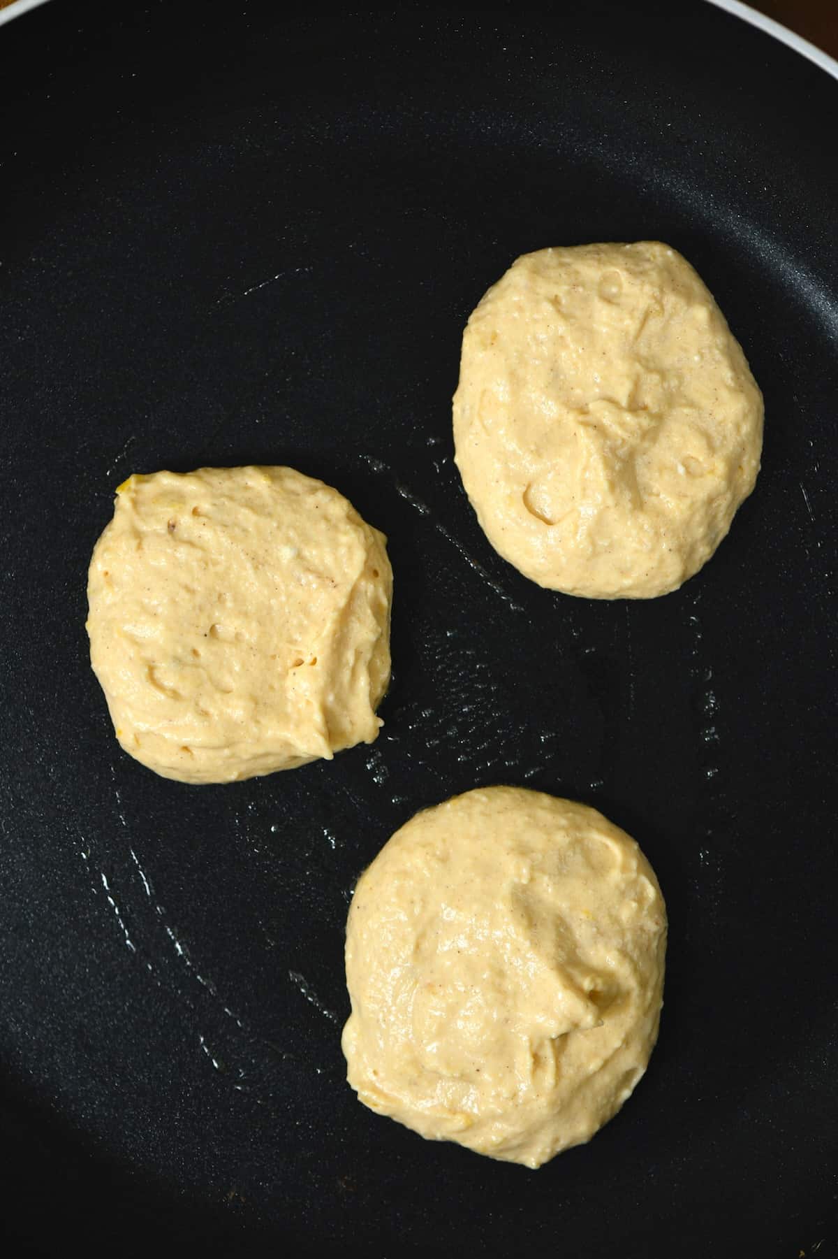 Three scoops of pancake batter on a pan