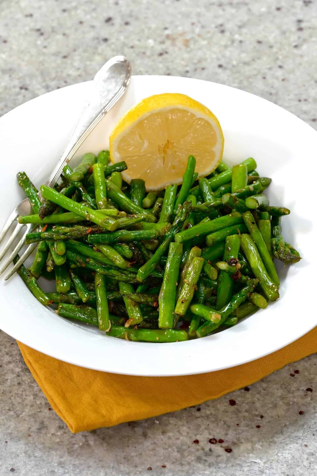 A serving of sautéed asparagus with a lemon slice in a white plate