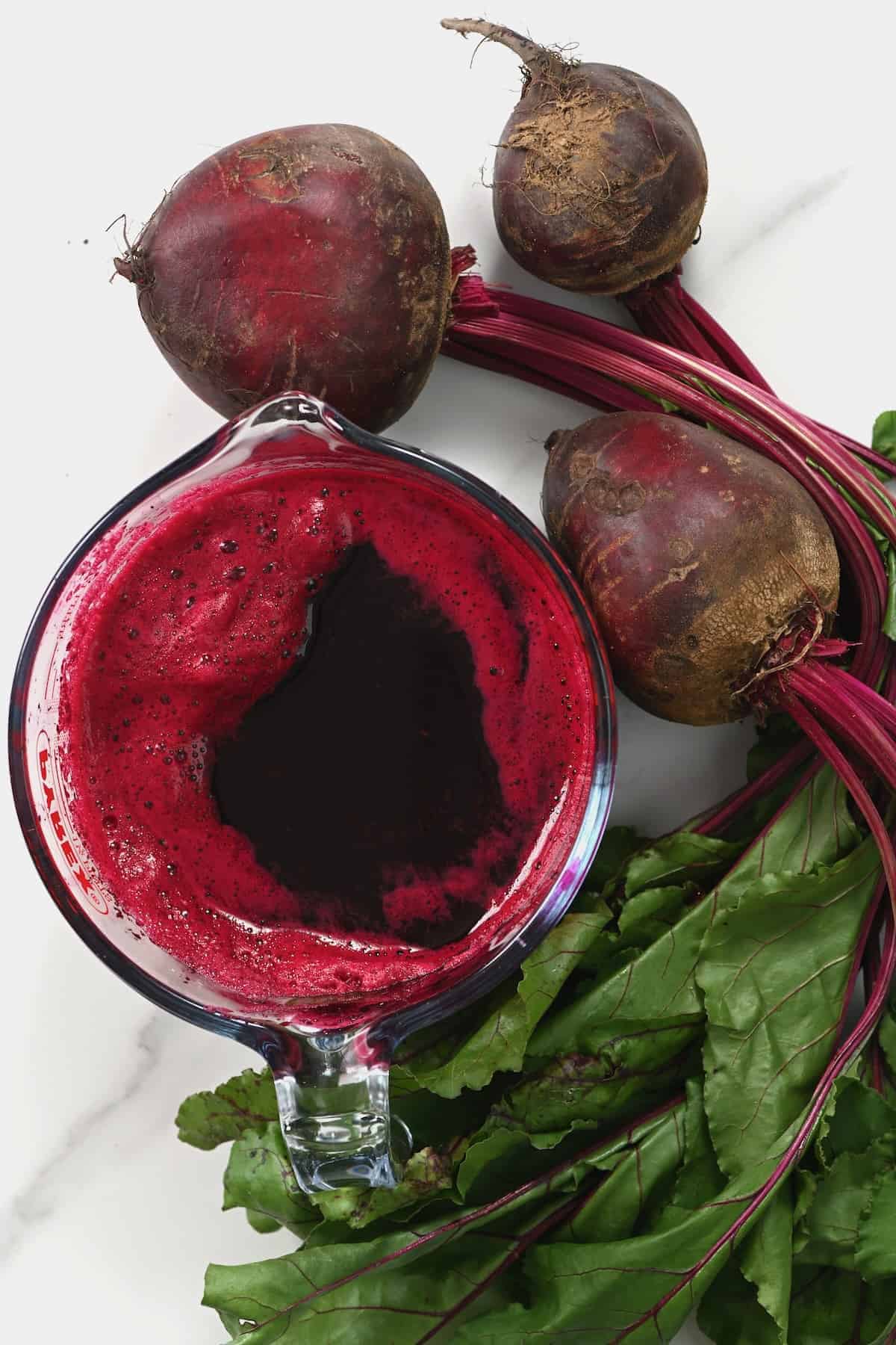 A large measuring cup with beet juice and three beets next to it
