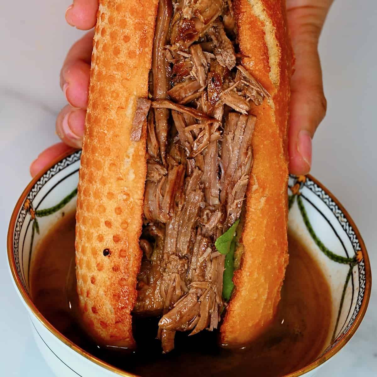 French dip sandwich being dipped into sauce