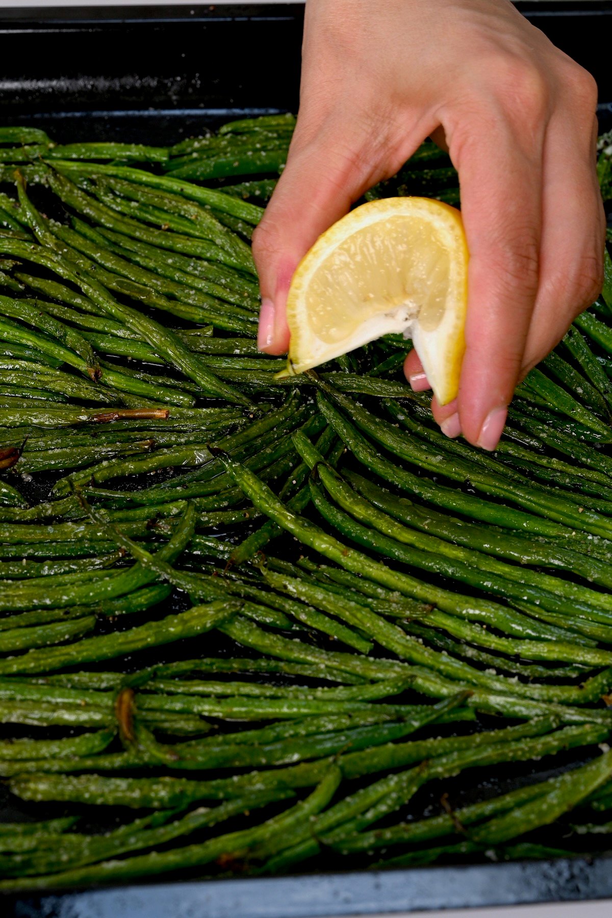 Lemon juice being drizzled over roasted green beans