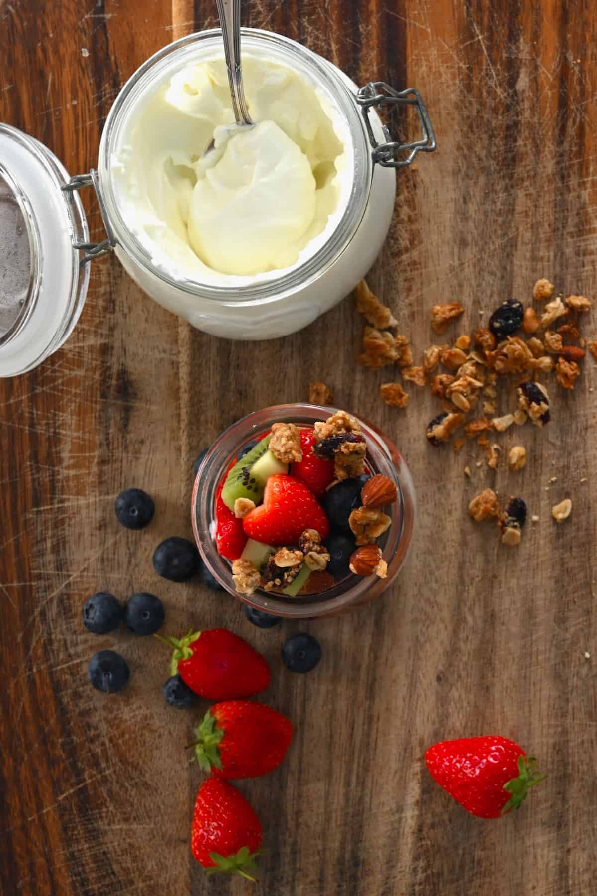 Yogurt parfait placed next to a bowl with yogurt and scattered berries