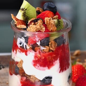 A small glass cup with yogurt parfait topped with berries and kiwi