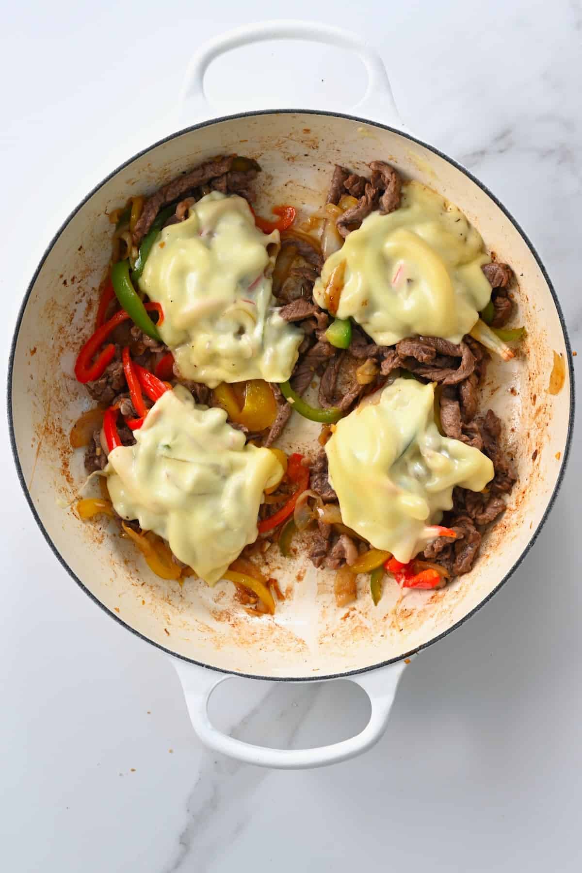 Cheese slices added over meat patties in a pan