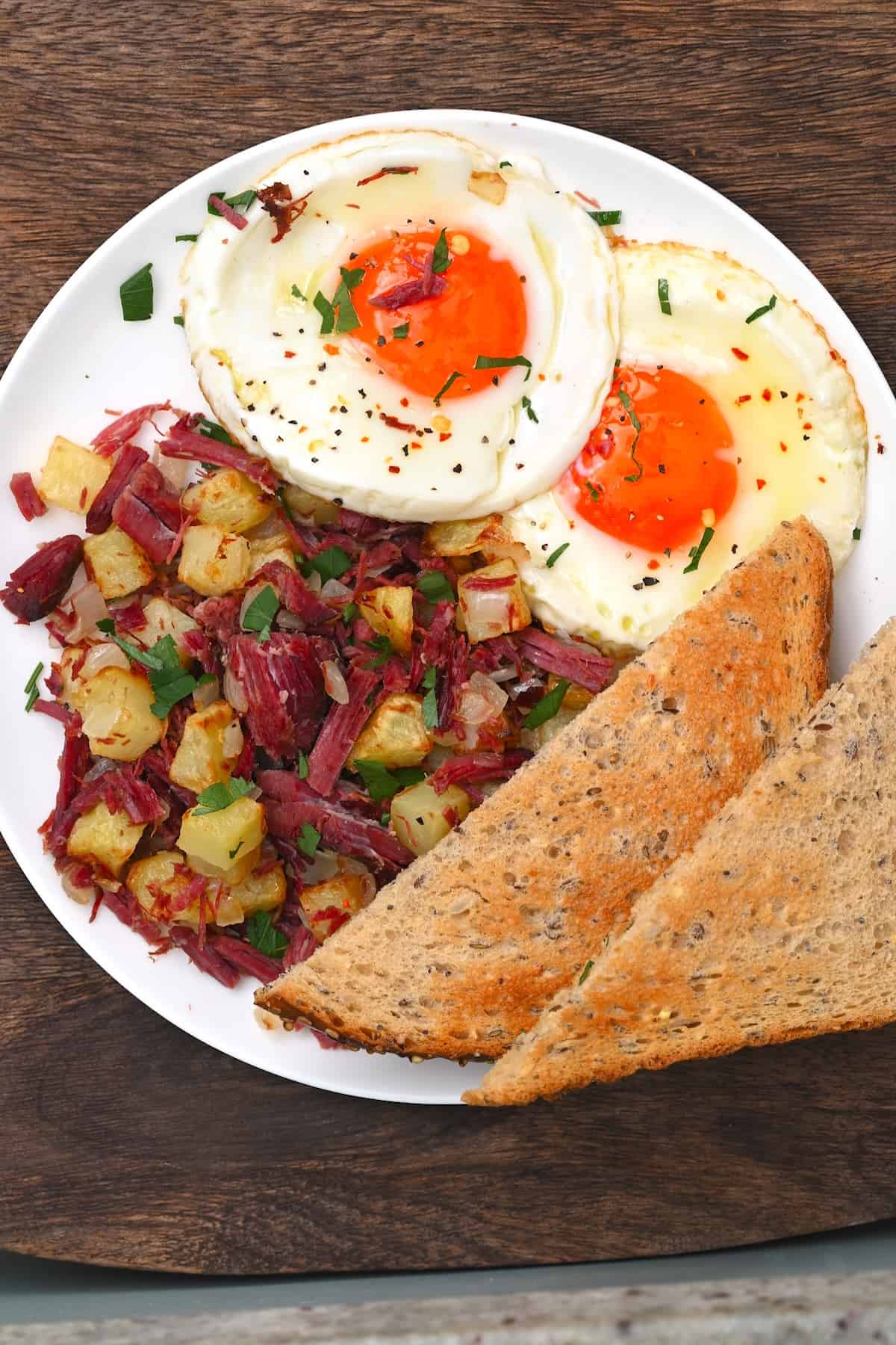 A serving of corned beef hash with fried eggs and bread