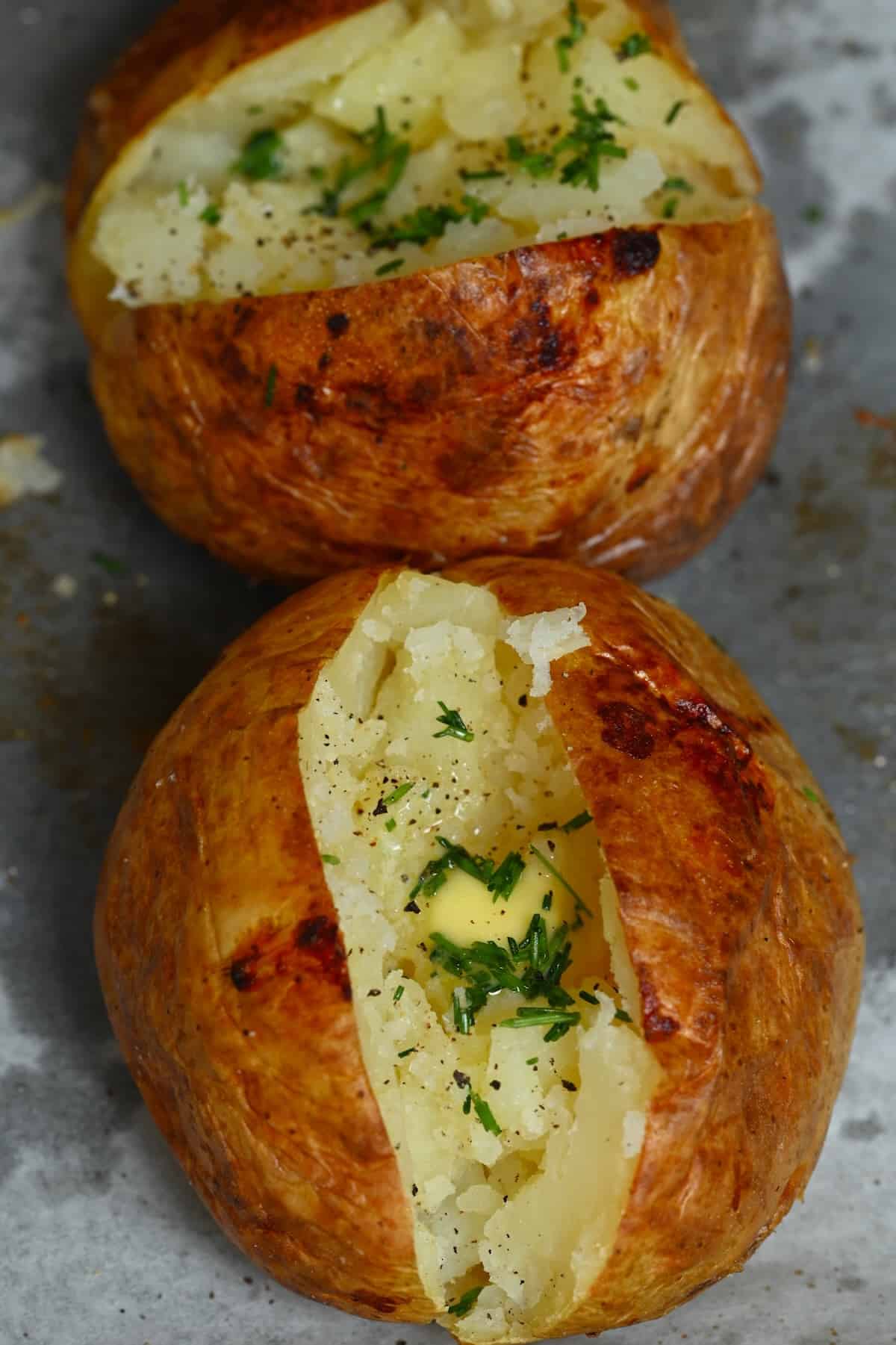 Two baked potatoes topped with butter and chives